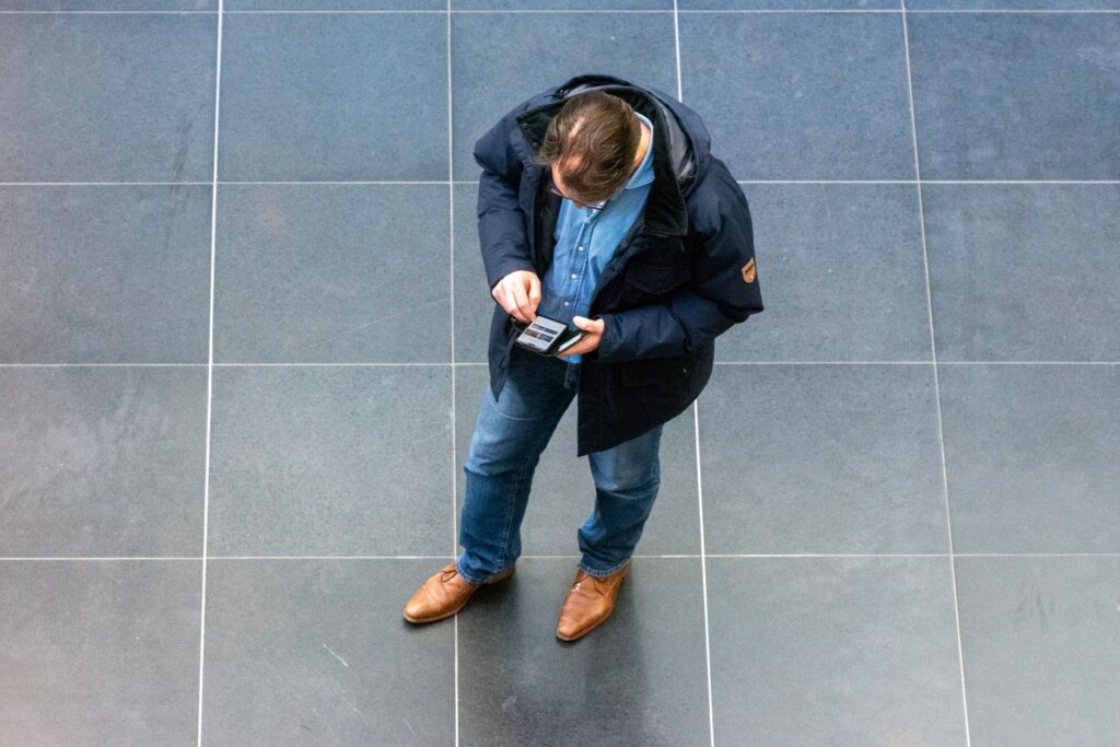 Tiler reviewing a job quote on a smartphone while kneeling beside freshly laid floor tiles on a residential project