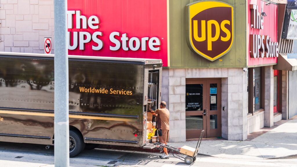 Person loading landscaping equipment into a branded pickup truck, USA residential street in background