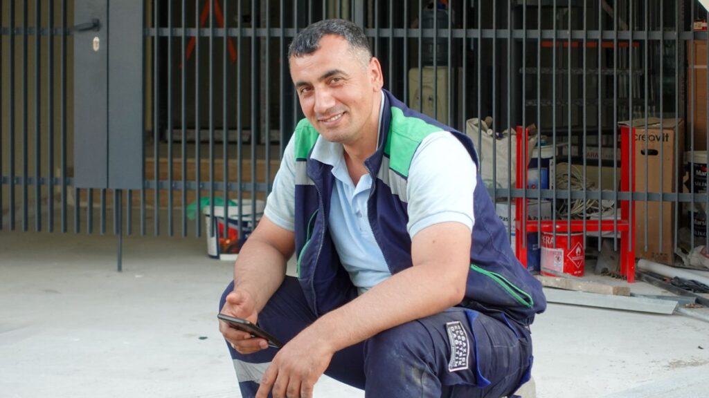 Bricklayer contractor reviewing a job quote on a smartphone at a US job site, professional workwear and tools visible