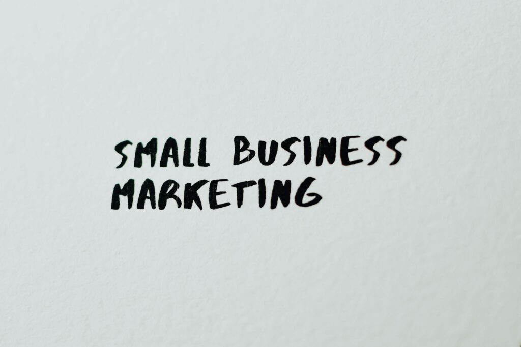 A small business owner sending a text message marketing campaign from a laptop, phone on the desk showing message preview