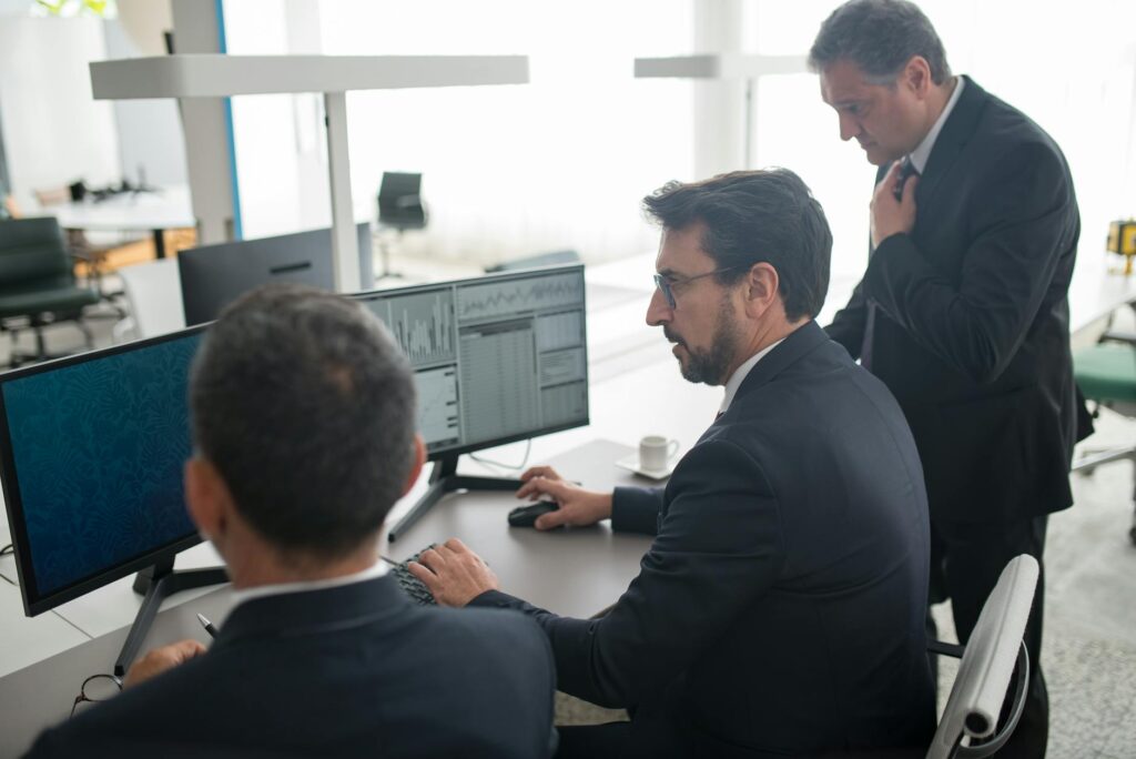 A trade business owner reviewing a job management system on a large monitor in a home office, trade vehicles visible outside