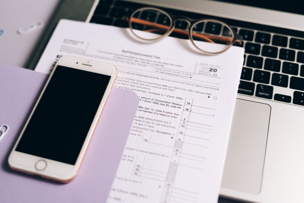 Self-employed US contractor reviewing tax documents on a phone and laptop at a desk